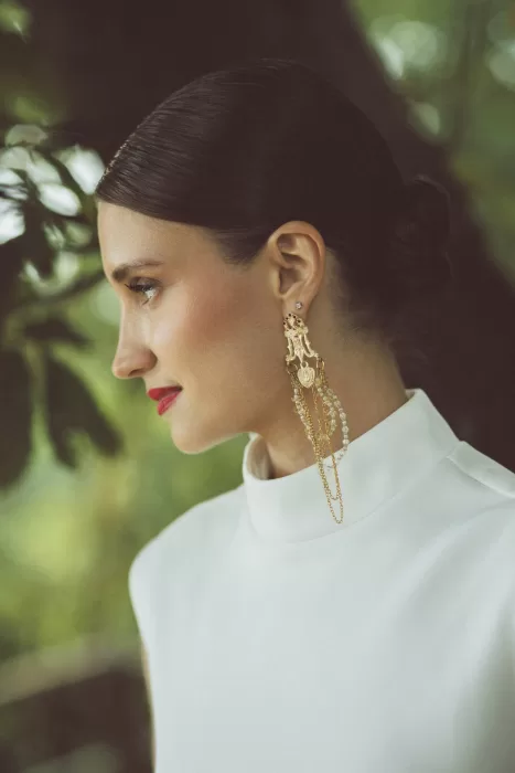 Close-up bridal portrait in white dress with statement gold earrings at Hotel Ristorante La Darsena surrounded by greenery.
