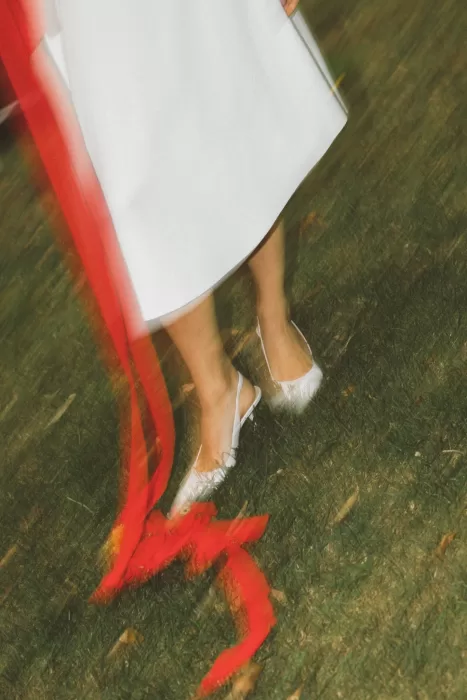 Bride walking across grass at Hotel Ristorante La Darsena, white heels and flowing red ribbons creating a soft, cinematic movement.