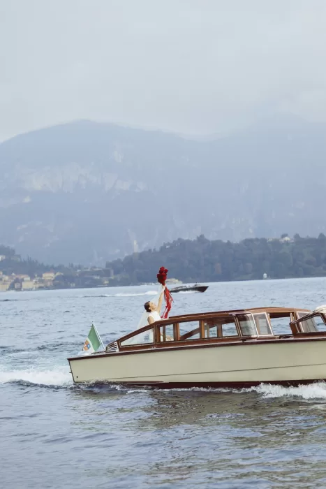 Bride lifting bouquet while cruising across Lake Como in classic wooden boat near Hotel Ristorante La Darsena.