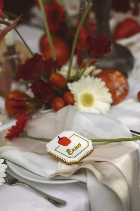 Elegant wedding place setting with personalised cookie, red florals and tomatoes at Hotel Ristorante La Darsena.