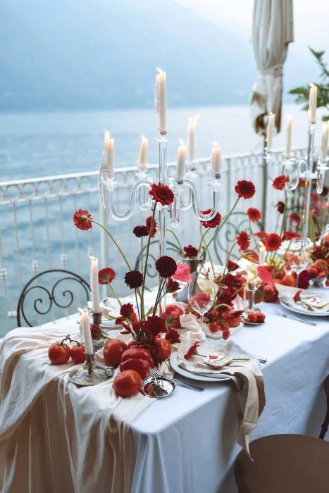Reception table styled with red flowers, candles and fresh tomatoes on lakeside terrace at Hotel Ristorante La Darsena.