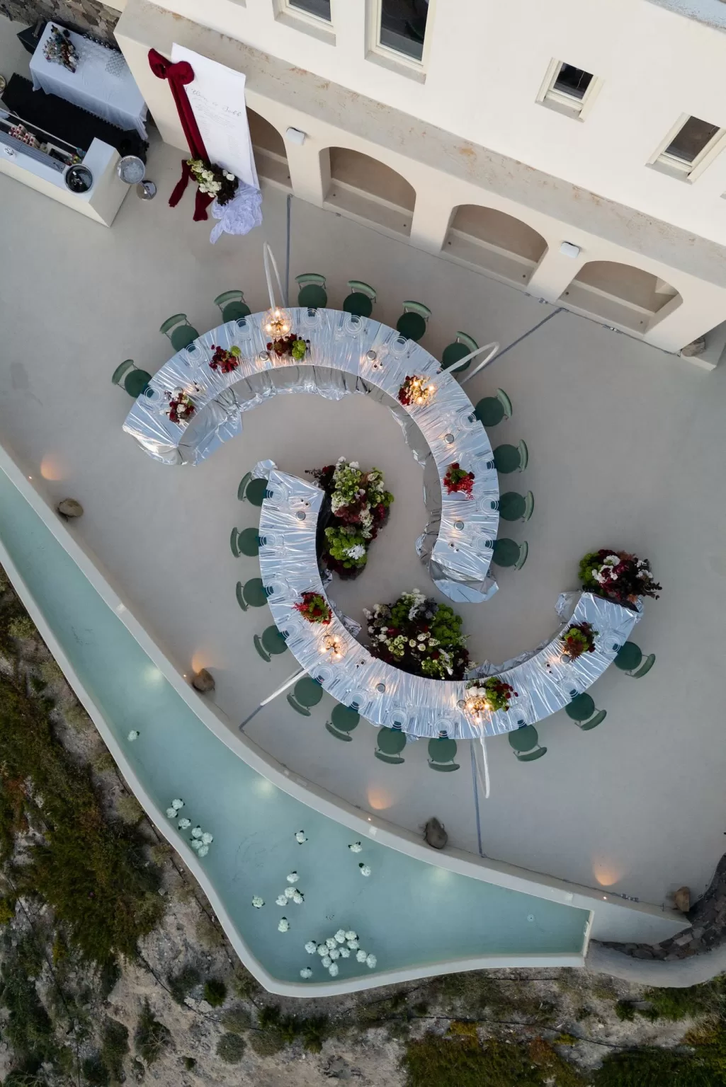 Overhead view of a curved wedding reception layout with floral installations and water features at Islet Santorini.