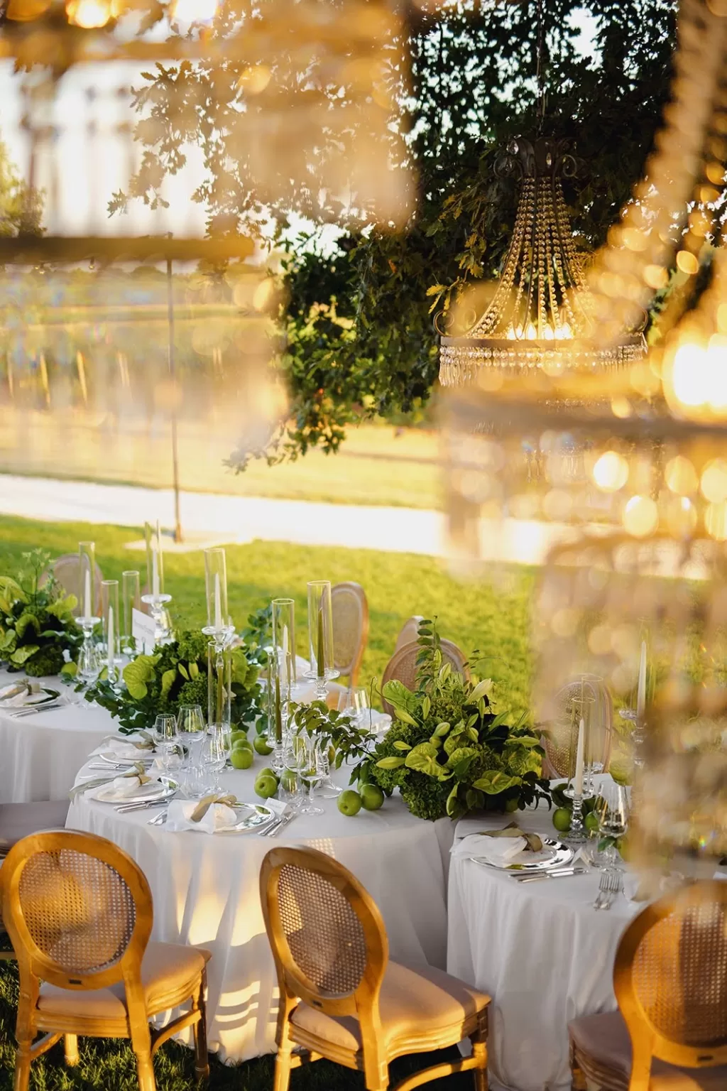 Elegant wedding table setup with greenery, candles, and chandeliers under trees at Meneghetti Wine Hotel.