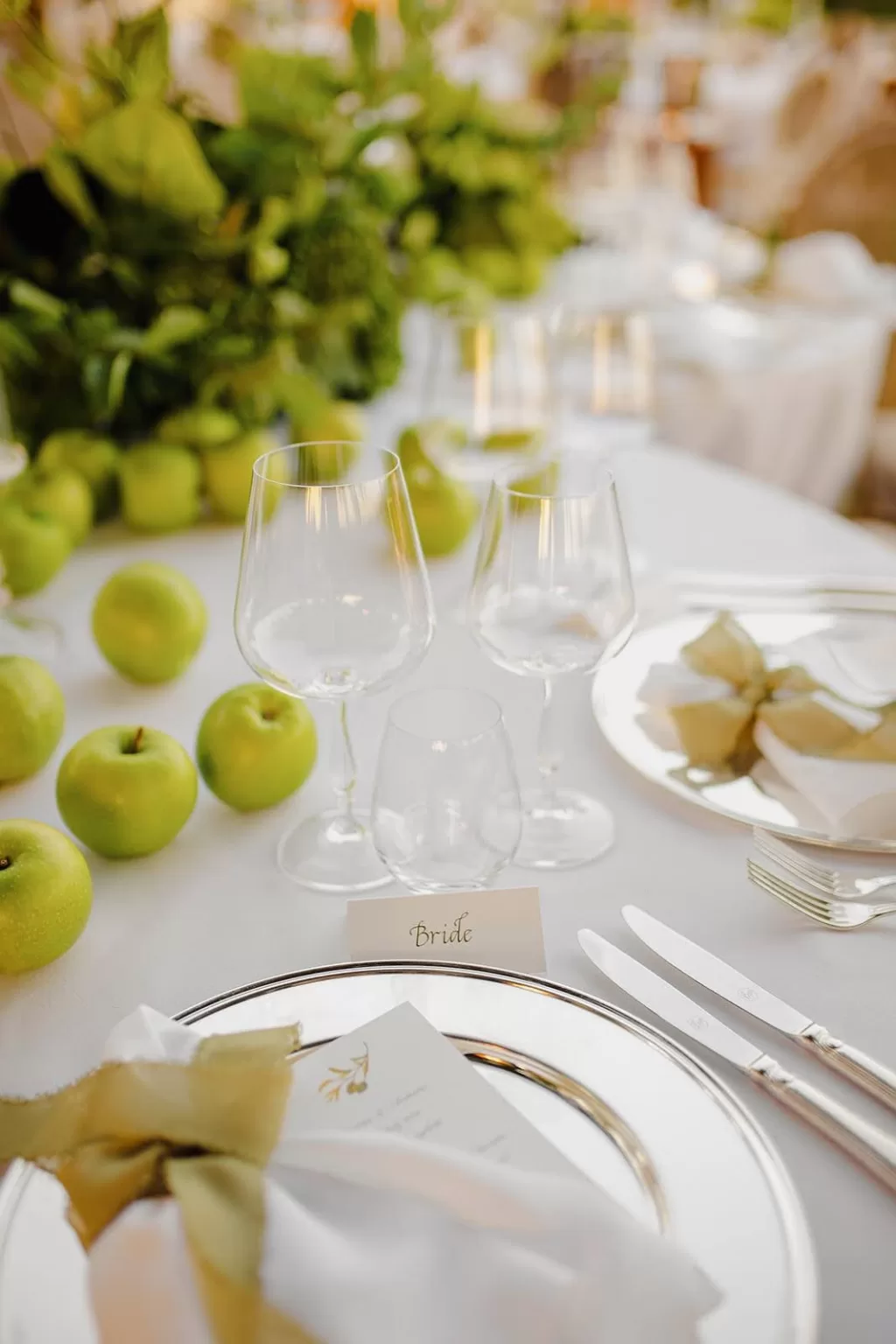 Elegant wedding table setting at Meneghetti Wine Hotel with green apples, fine glassware, and soft natural light.
