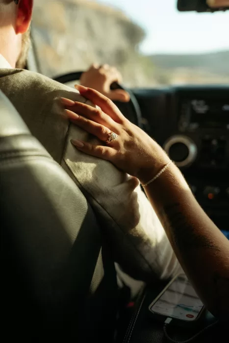 Bride’s hand with engagement ring resting on groom’s shoulder during scenic coastal drive near Milos Cove.