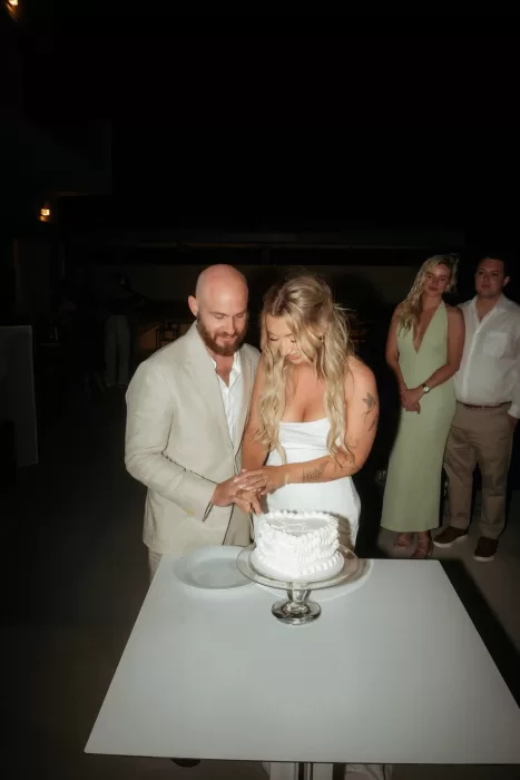Bride and groom cutting wedding cake during evening celebration at Milos Cove.