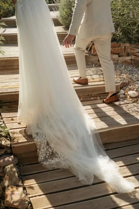 Close-up of bride’s flowing veil and groom walking up wooden steps at Milos Cove garden pathways.