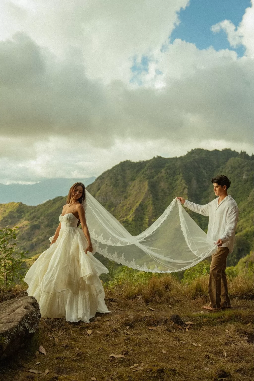 Groom holding the bride’s long veil across a mountain clearing near Ossipoff’s Cabin, highlighting scale and scenery.