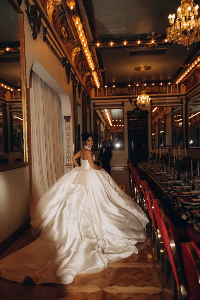 Bride smiling over her shoulder as her dramatic satin gown sweeps through the grand ballroom of Palacio Metropolitano.