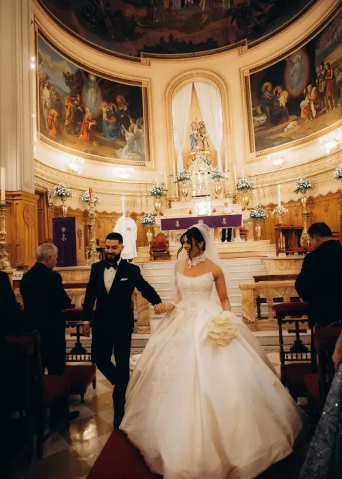 Newlyweds walking down the aisle inside the grand chapel of Palacio Metropolitano beneath frescoed ceilings and floral arrangements.