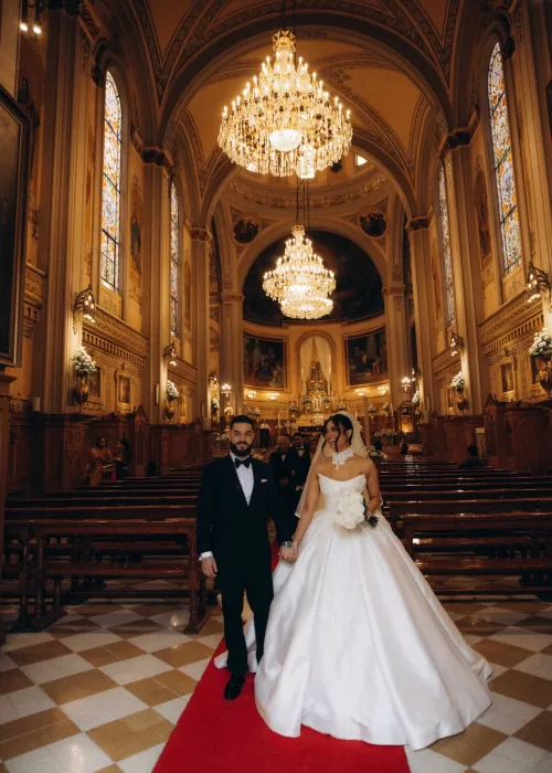 Newlyweds walking down the red aisle inside Palacio Metropolitano’s grand chapel beneath towering chandeliers and stained glass windows.