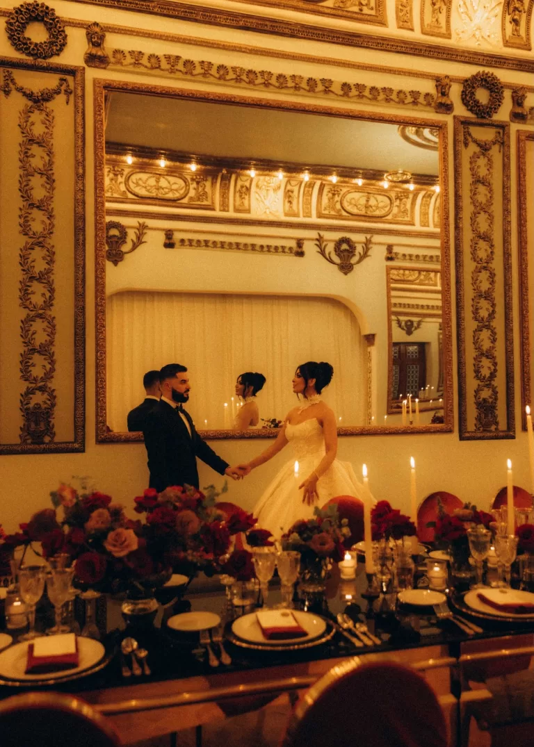 Bride and groom holding hands in the gilded ballroom of Palacio Metropolitano with mirrored walls and chandeliers glowing above.