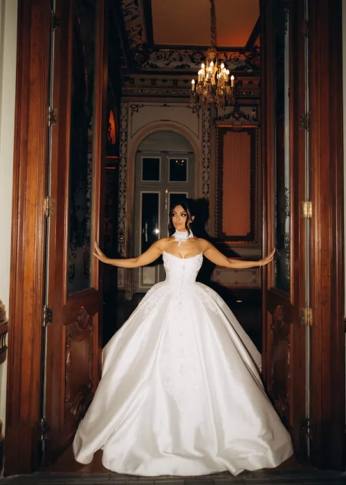 Bride framed by tall wooden doors at Palacio Metropolitano, her structured gown illuminated by warm chandelier light.