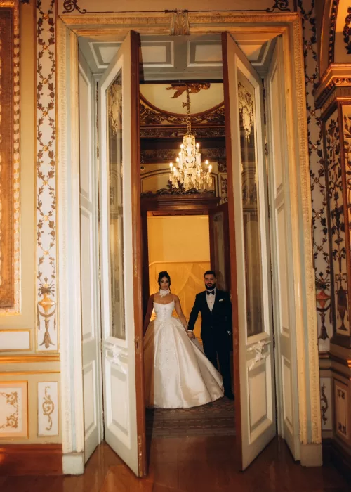 Bride and groom standing in the ornate doorway of Palacio Metropolitano beneath crystal chandeliers and gilded detailing.