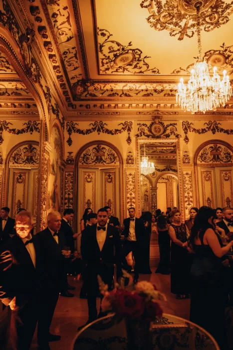 Wedding guests mingling beneath crystal chandeliers in the ornate gold grand salon of Palacio Metropolitano.