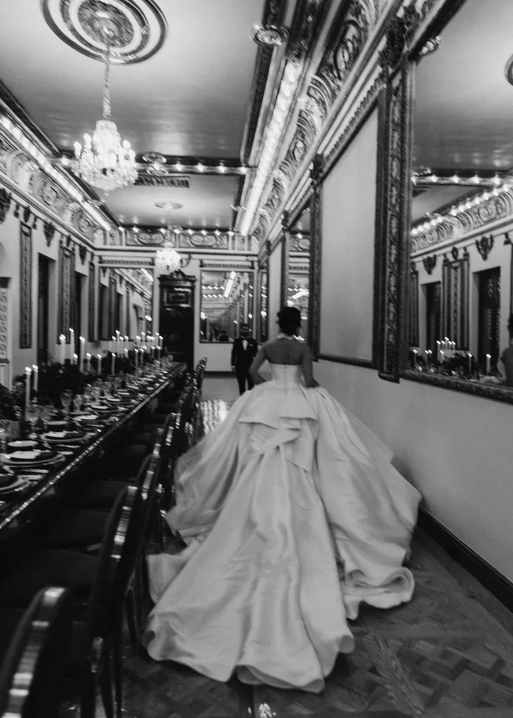 Bride walking through the candlelit reception hall at Palacio Metropolitano with long banquet tables and chandeliers overhead.