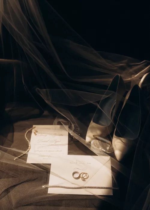 Wedding invitation suite, rings and bridal heels styled beneath a veil at Palacio Metropolitano in soft evening light.