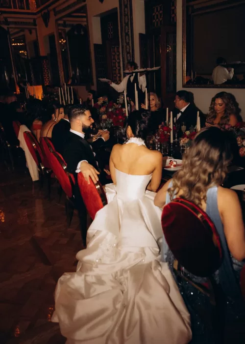 Guests seated at an intimate candlelit wedding dinner at Palacio Metropolitano surrounded by rich red florals and velvet chairs.