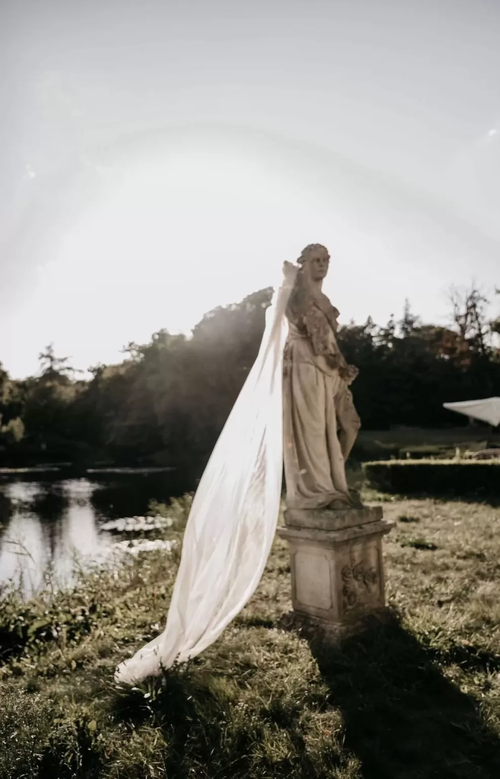 Bride’s flowing veil draped across a classical garden statue at Parc Broekhuizen.
