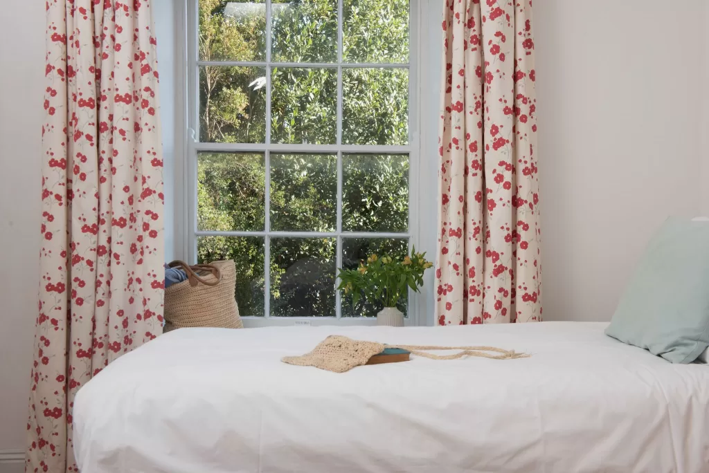 Bright bedroom at Scorrier House with white bedding and floral curtains framing a garden view.
