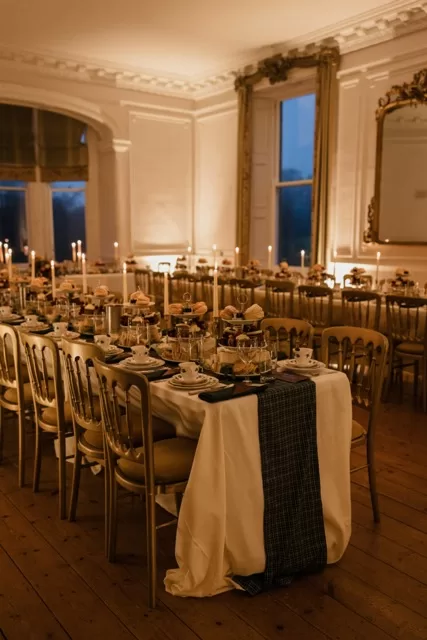 Long candlelit dining table set for a wedding breakfast inside Scorrier House with elegant place settings.