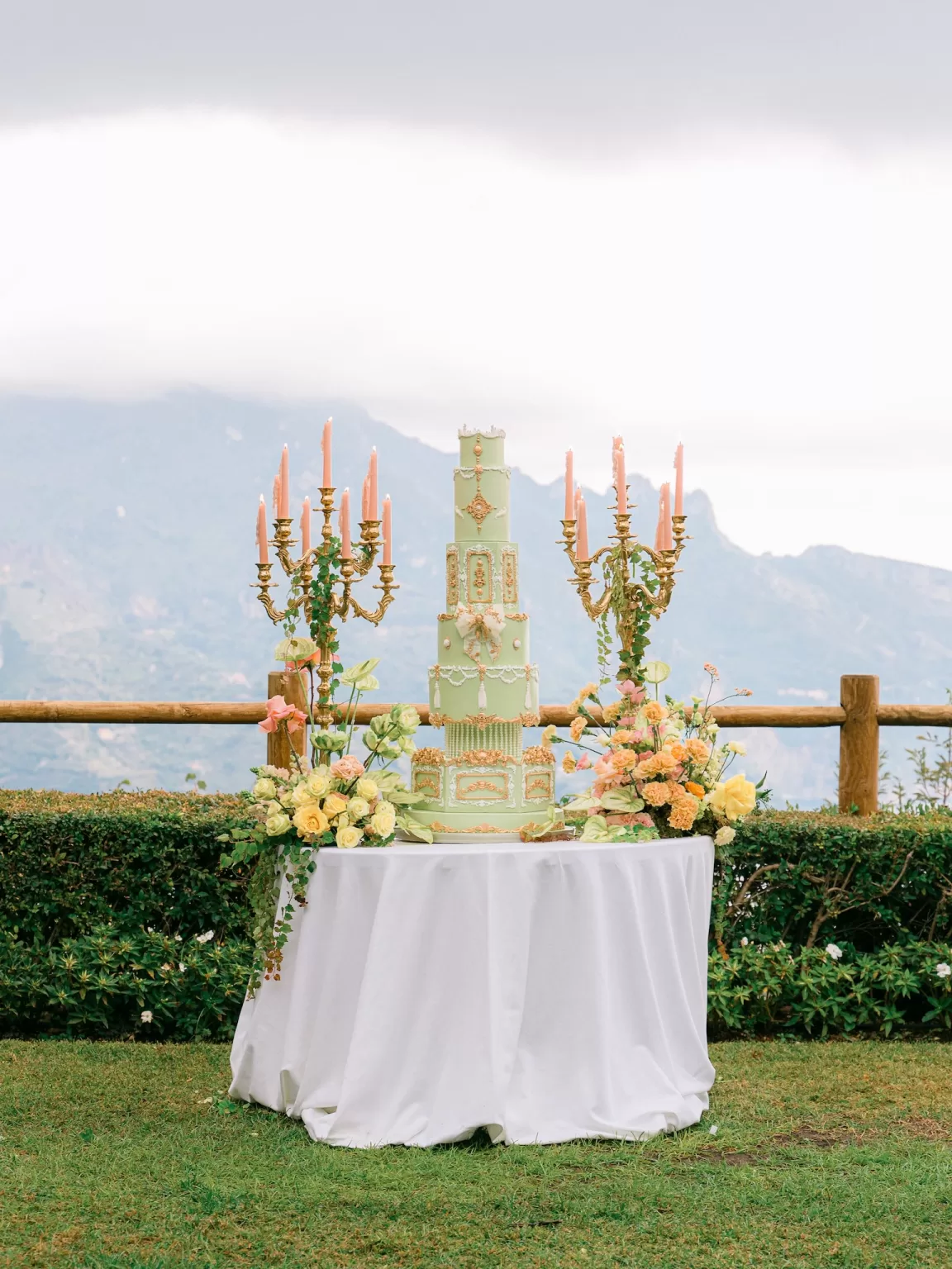 Grand pastel green wedding cake with gold details and chandeliers overlooking mountain views, photographed by Sim Sawyers Photography