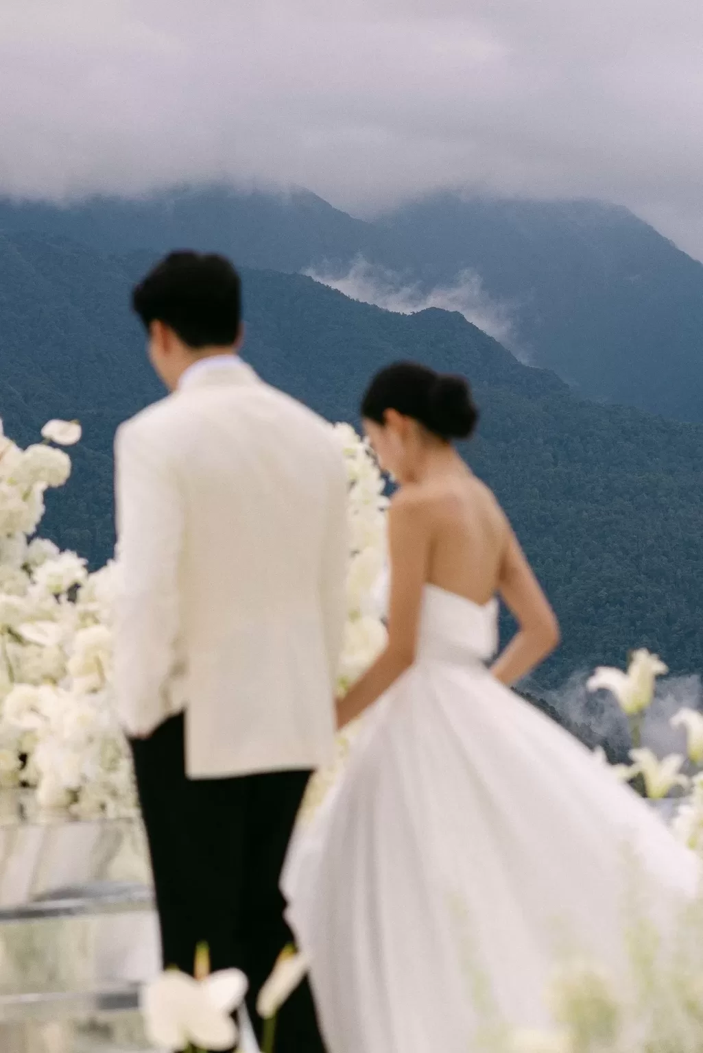 Bride and groom walking across a white floral ceremony platform with misty mountain backdrop at Ville de Mont Mountain Resort.