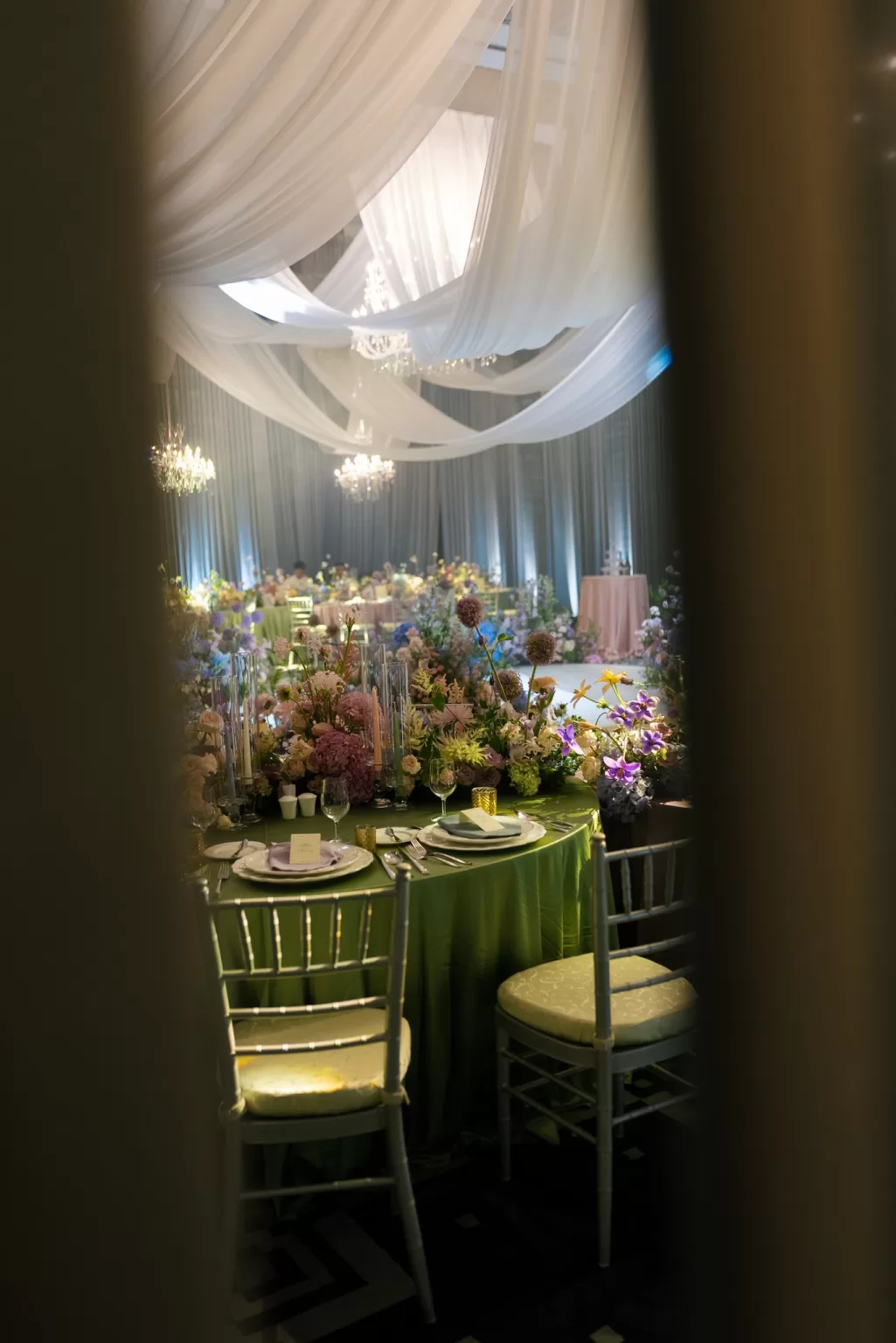 Reception tables styled with colourful florals beneath soft cascading drapery and chandeliers at Ville de Mont Mountain Resort.