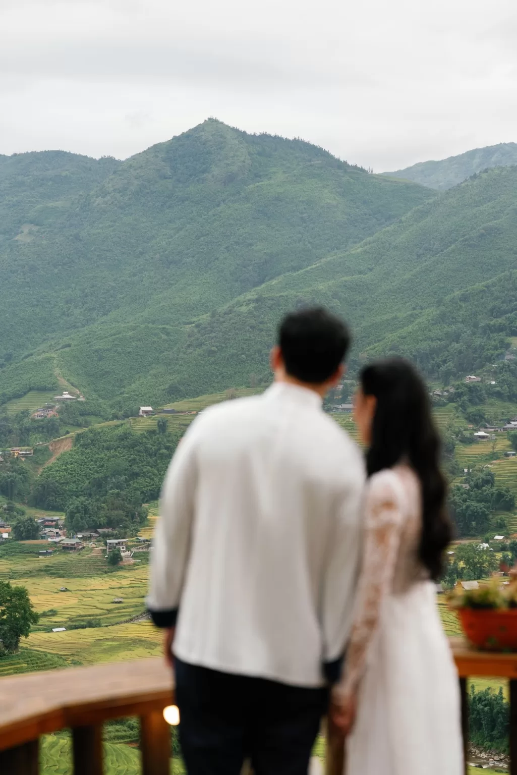 Couple overlooking lush terraced mountains from a balcony at Ville de Mont Mountain Resort, surrounded by soft green hills and misty valley views.