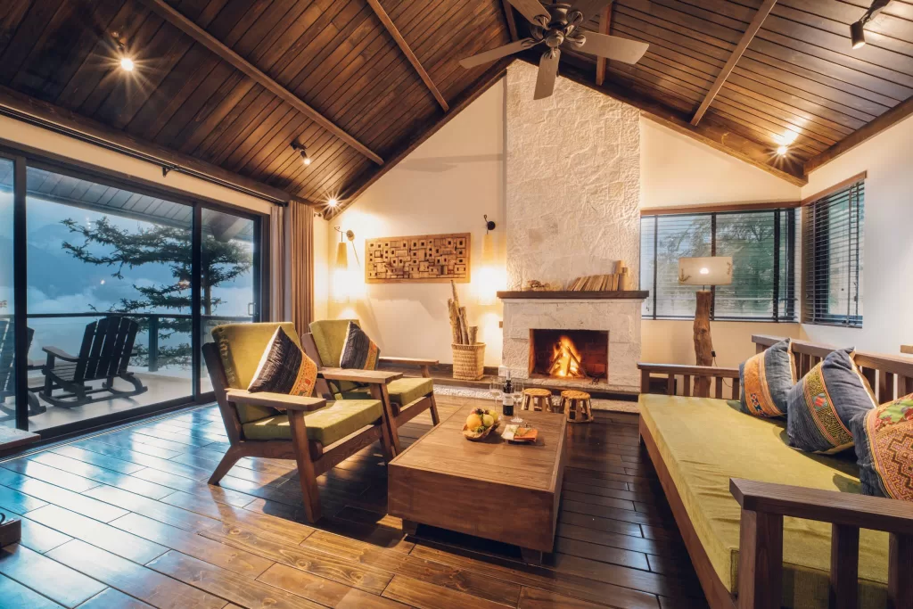 Warm villa living room at Ville De Mont Mountain Resort with fireplace, wooden interiors, and mountain views through large windows.
