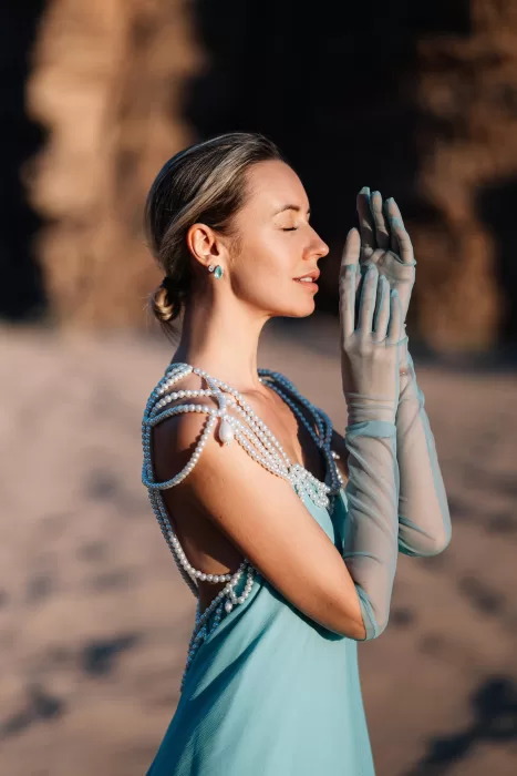 Close portrait of bride in pearl-embellished blue gown and sheer gloves, standing in golden Wadi Rum desert light.
