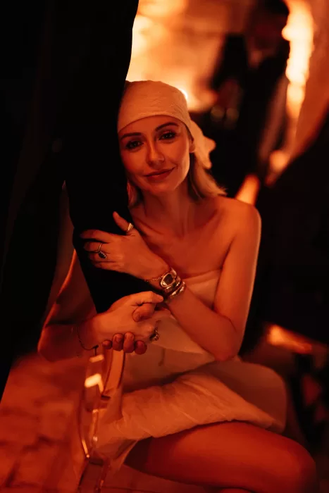 Bride seated in warm candlelight at Wadi Rum reception, wearing a modern white mini dress and headscarf, holding her partner’s hand.