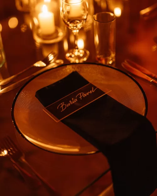 Elegant candlelit place setting at Wadi Rum wedding reception with black napkin, glass charger plate and warm amber lighting.