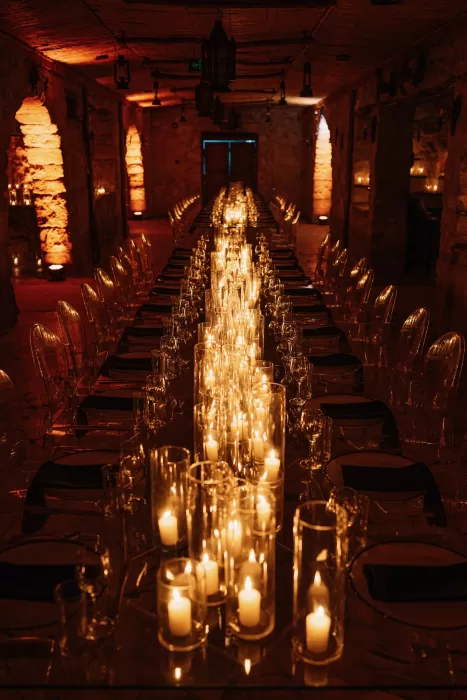Candlelit reception hall in Wadi Rum with long glass tables and glowing pillar candles creating a warm, intimate evening atmosphere.