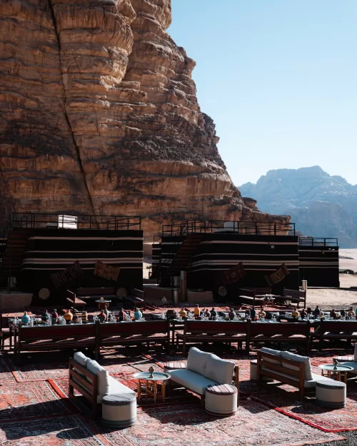 Luxury desert camp reception setup at Wadi Rum with patterned rugs, lounge seating and long banquet tables beneath towering cliffs.
