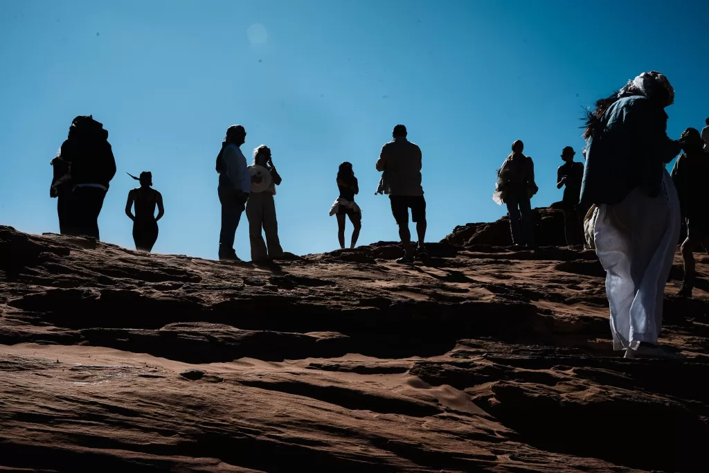 Wedding guests silhouetted against clear blue sky on rocky ridge in Wadi Rum, capturing the vast scale of the desert landscape.