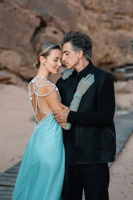Bride and groom embracing in Wadi Rum at dusk, her pearl-embellished gown contrasting his dark tailored look.