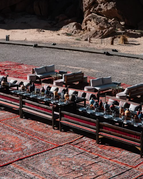 Overhead view of long reception tables arranged on richly patterned rugs in Wadi Rum desert, styled with ceramic vases and silverware.