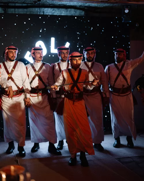 Traditional Jordanian dabke dancers performing at Wadi Rum wedding reception, wearing white thobes and red keffiyeh headscarves.