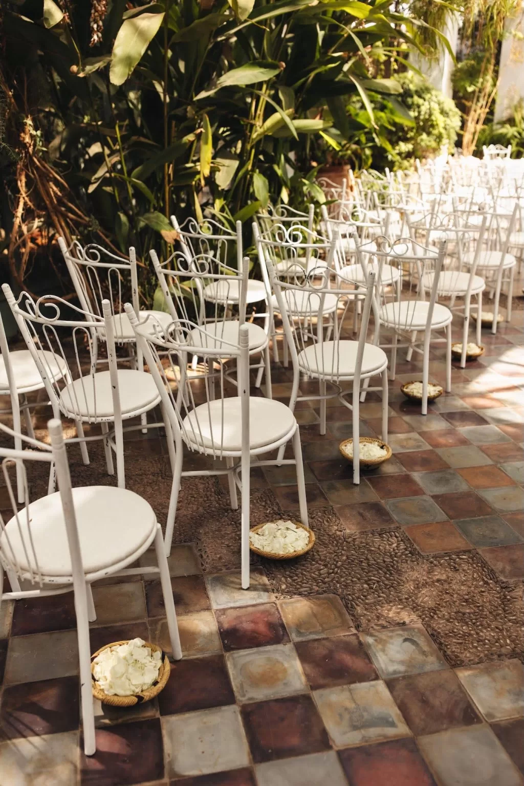 Ceremony setup inside the glasshouse at Beldi Country Club, with white chairs, chandeliers, and a floral arch under natural light.