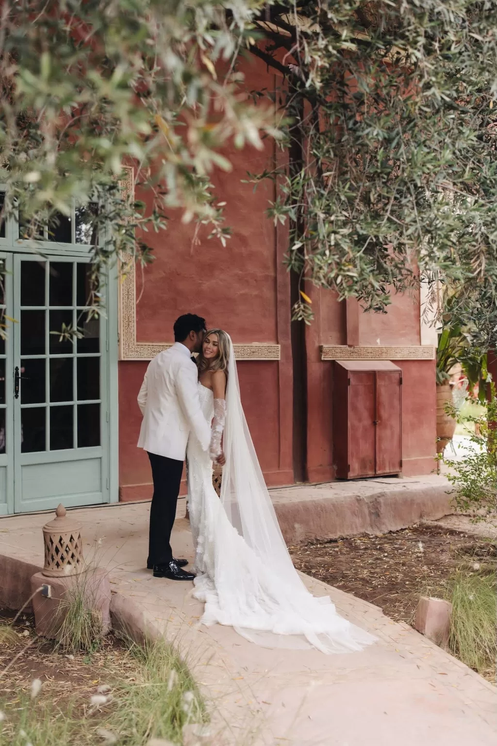 Bride and groom embracing under olive branches beside terracotta walls at Beldi Country Club.