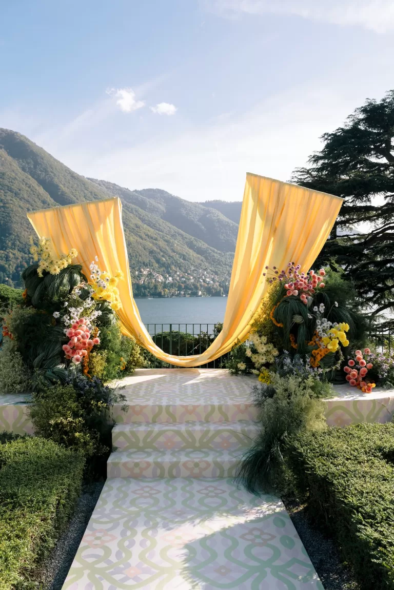 Lake Como wedding ceremony altar with flowing yellow drapery and vibrant florals overlooking the mountains and water, designed by Benevent Planner.