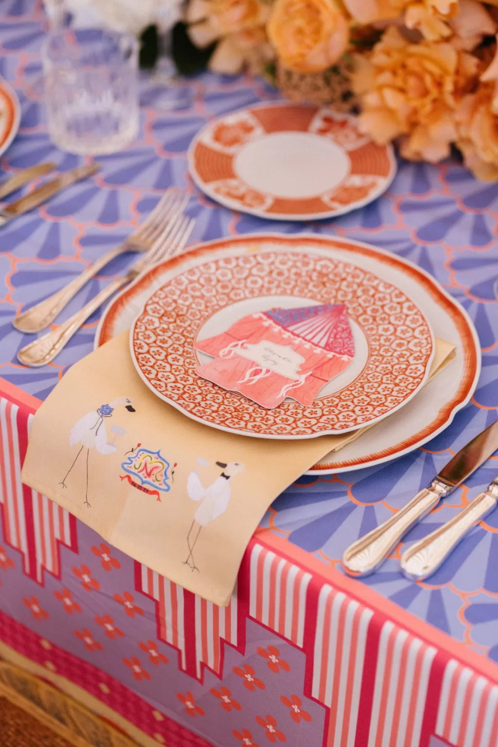 Close-up of a colourful wedding table setting with patterned linens, illustrated napkin and decorative china styled for a Benevent Planner celebration.