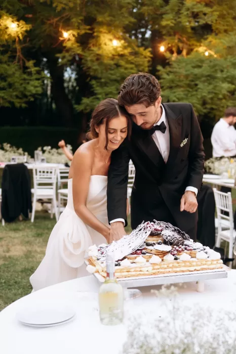 Bride and groom cutting wedding cake outdoors under string lights at Castello di San Fabiano
