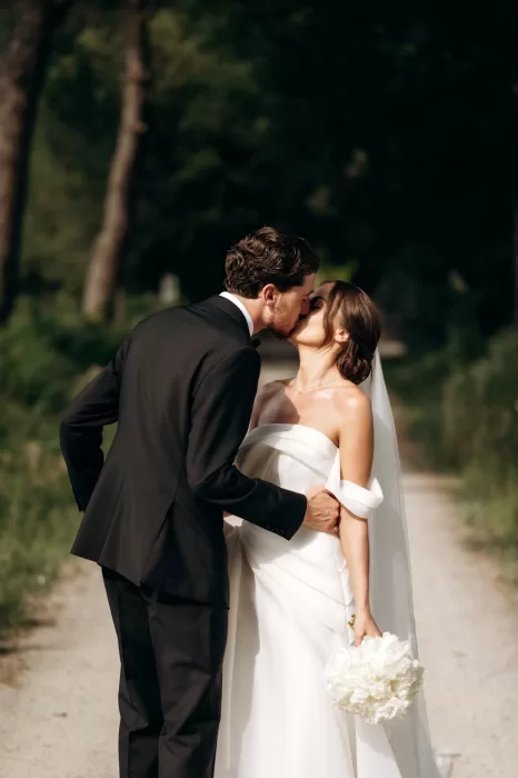 Couple kissing on sunlit pathway at Castello di San Fabiano surrounded by greenery and soft light