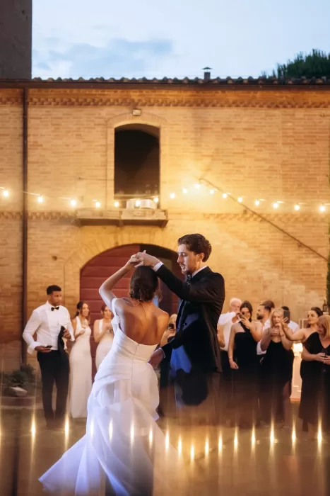 Couple sharing first dance surrounded by guests and warm lights at Castello di San Fabiano