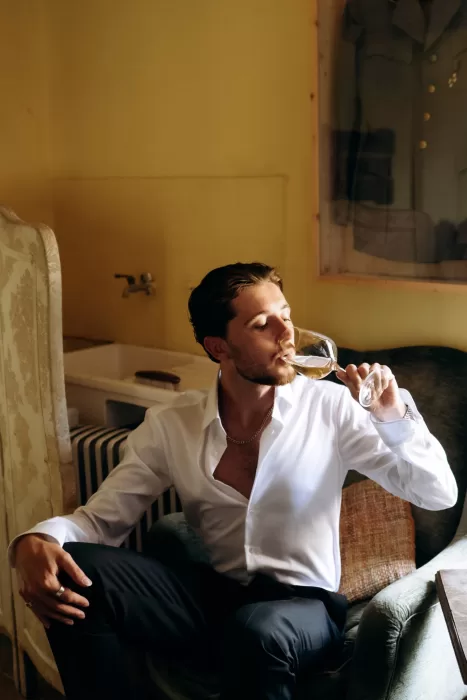 Groom sitting in armchair drinking champagne during preparations at Castello di San Fabiano
