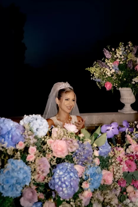 Bride smiling during the evening reception behind abundant pastel floral centrepieces at Château Bouffémont.