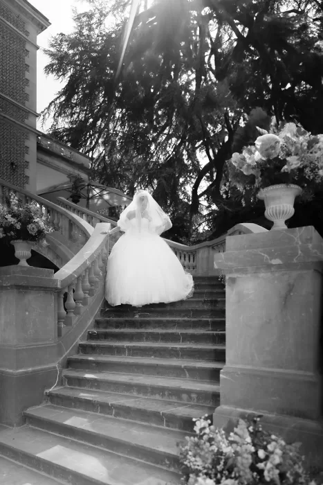 Bride descending the stone staircase with flowing veil and pastel floral arrangements at Château Bouffémont.