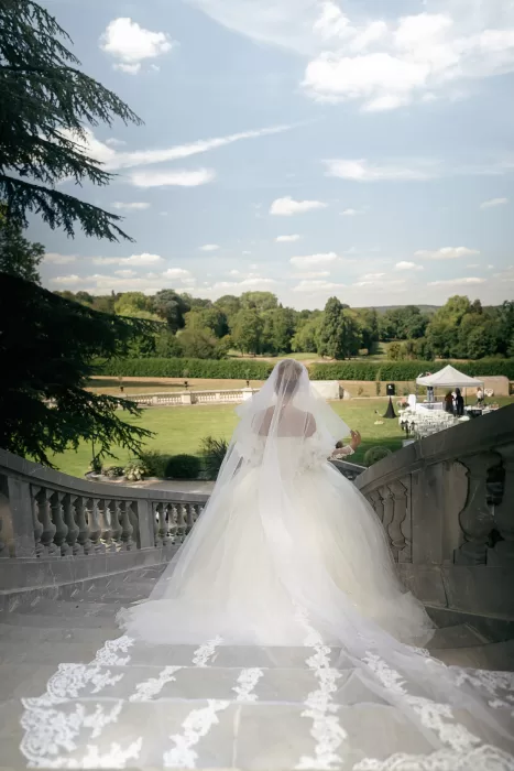 Bride descending the stone staircase with flowing veil and pastel floral arrangements at Château Bouffémont.